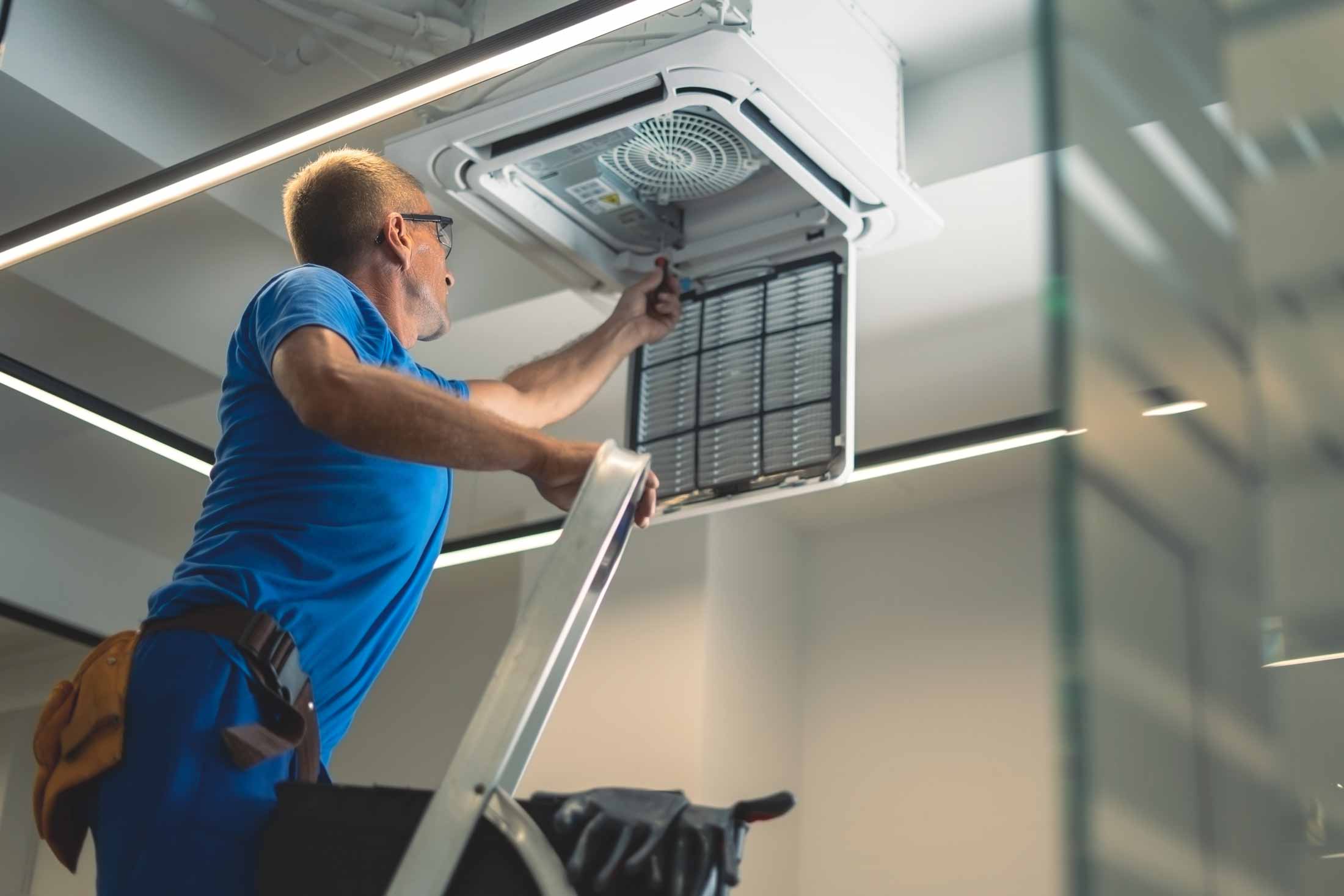 Technician inspecting a ceiling-mounted HVAC unit during maintenance